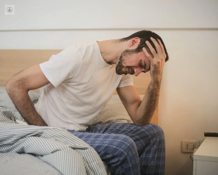 Chico sentado en una cama, sujetándose la cabeza, en actitud de dolor - endourología - by Top Doctors
