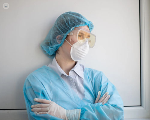 Mujer mirando al infinito, con macarilla, gafas y traje de seguridad - covid persistente - by Top Doctors