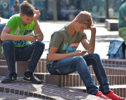 Adolescentes mirando el móvil sentados en la calle - autolesiones adolescentes - by Top Doctors