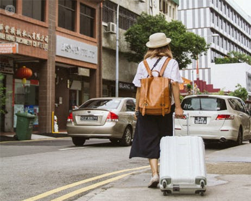 Encuadre por detrás de una chica en una ciudad, con una maleta y una mochila - vivir en el extranjero - by Top Doctors