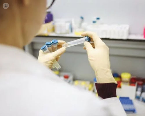 Mujer de espaldas en un laboratorio con diversos tubos en la mano - cura coronavirus - COVID-19 - by Top Doctors