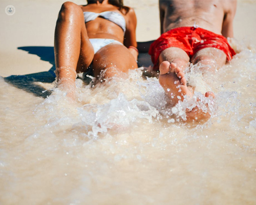 Chico y chica tomando el sol en la playa - riesgo de cáncer de piel by Top Doctors