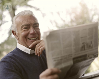 hombre sonrie mientras lee el periódico