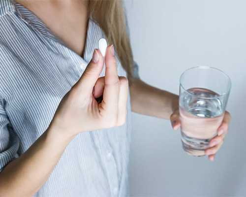 Chica tomándose una pastilla con un vaso de agua en la mano - alergia a medicamentos - by Top Doctors
