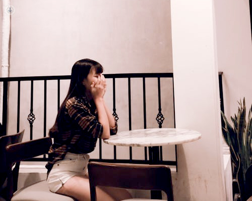 Chica sentada en una mesa, triste y tapándose la cara - anticipación negativa - by Top Doctors