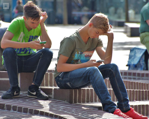 Adolescentes sentados en una escalinata mirando el móvil - Adicción a las nuevas tecnologías - by Top Doctors