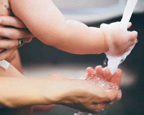 Manos de un niño y una persona adulta, ayudándole a lavarse las manos - sabañones y COVID - by Top Doctors