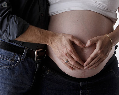 Primer plano de una tripa embarazada y un corazón hecho con las manos del padre y la madre - infertilidad - by Top Doctors