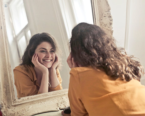 Chica mirándose al espejo y sonriendo - carillas dentales y ortodoncia - by Top Doctors
