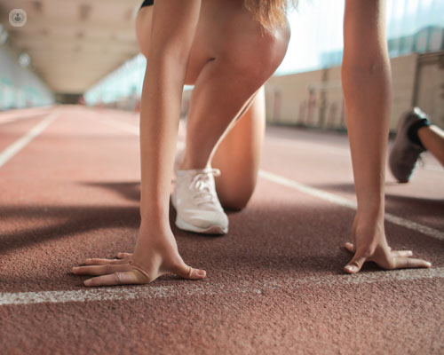 Primer plano de las manos y piernas de una chica en una pista de atletismo - mal entrenamiento y lesiones - by Top Doctors