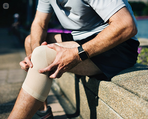 Primer plano de la pierna de un hombre con rodillera, agarrándose la rodilla - artroscopia de menisco - by Top Doctors