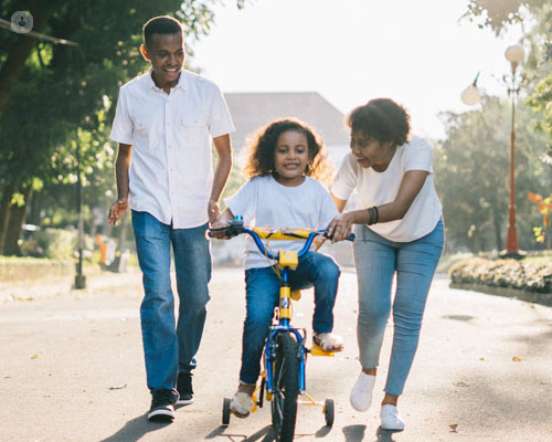 Pareja ayudando a una niña a montar en bicicleta - familia - adopción - by Top Doctors
