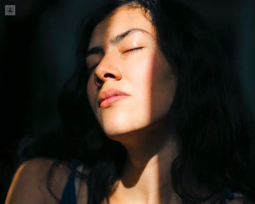 Chica con un rayo de sol en la cara, con gesto molesto - fotofobia by Top Doctors