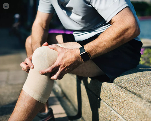Hombre sentado con una rodillera y tocándose la rodilla - fisioterapia deportiva - by Top Doctors