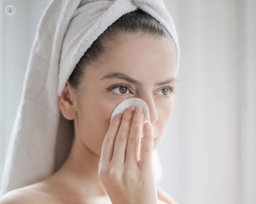 Primer plano de una chica limpiándose la cara con un algodón - acné - by Top Doctors