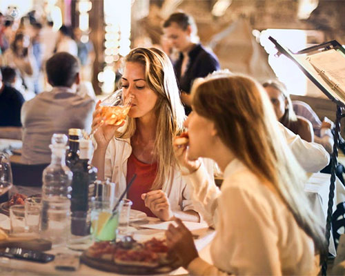 Dos chicas en una mesa de restaurante comiendo - alimentos a evitar si viajamos - by Top Doctors