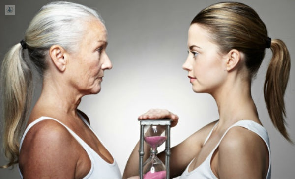Mujer mayor y chica joven frente a frente, con un reloj de arena en el centro como símbolo de paso del tiempo - piel es el reflejo del organismo - by Top Doctors