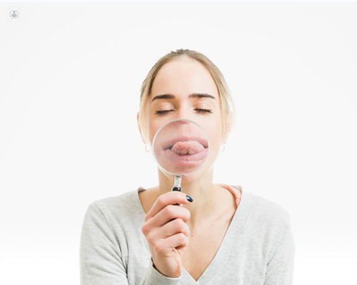 Chica mostrando la lengua y enfocándola con una lupa - enfermedades de la lengua by Top Doctors