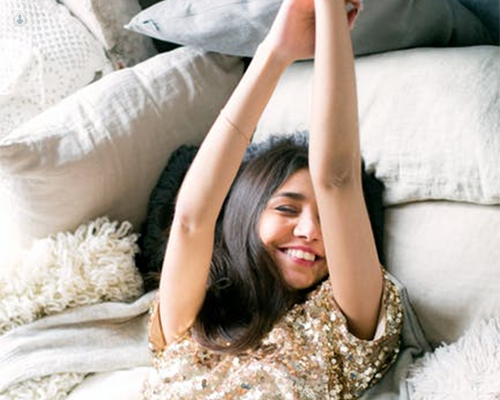Chica tumbada en una cama sonriendo, con los brazos hacia arriba - lifting de brazos - by Top Doctors