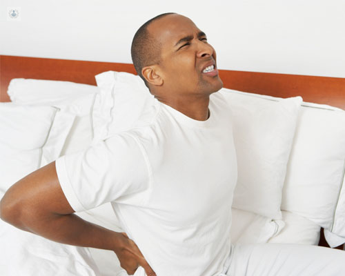 Hombre sentado en una cama tocándose las lumbares con cara de dolor - patologías de espalda - neurocirugía - técnica TLIF  by Top Doctors