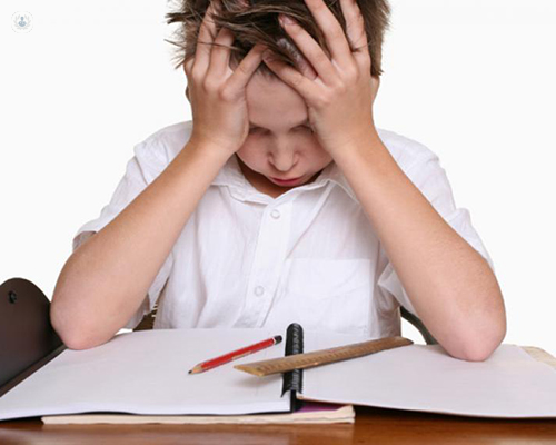 Primer plano de un niño en actitud de desesperación delante de una libreta o deberes - trastorno del aprendizaje - by Top Doctors
