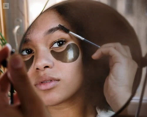 Chica mirándose en el espejo retocándose las cejas - implante de cejas by Top Doctors